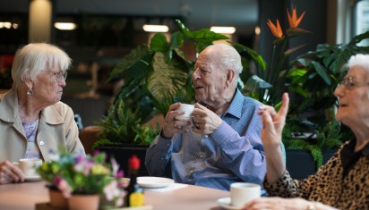 meneer drinkt zijn koffie aan tafel met andere bewoners
