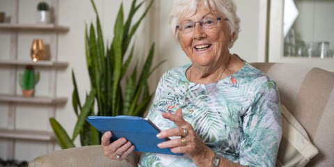 Dame met iPad in handen lacht in de camera