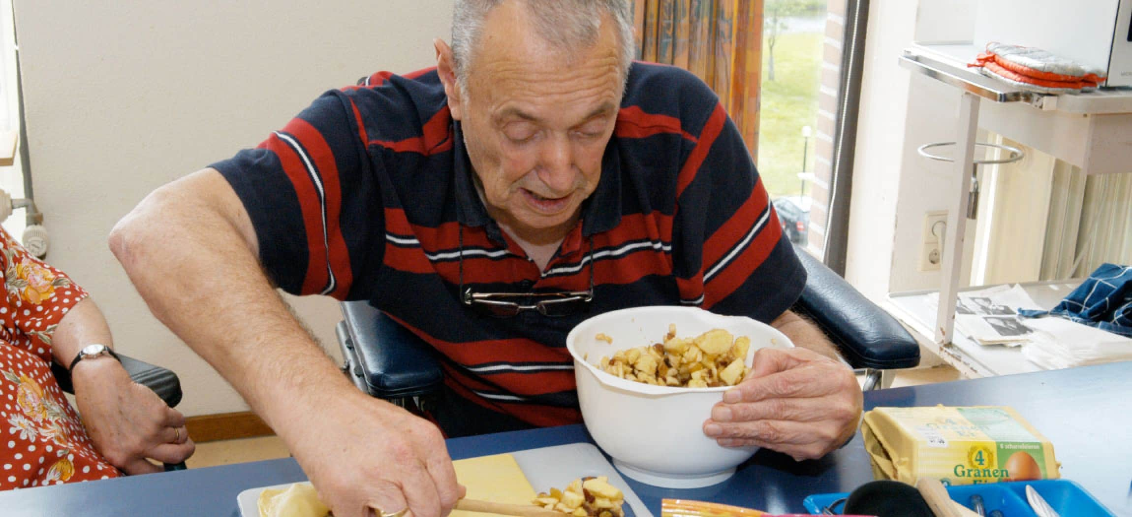 Opa maakt appelflappen aan tafel met kom appelpartjes