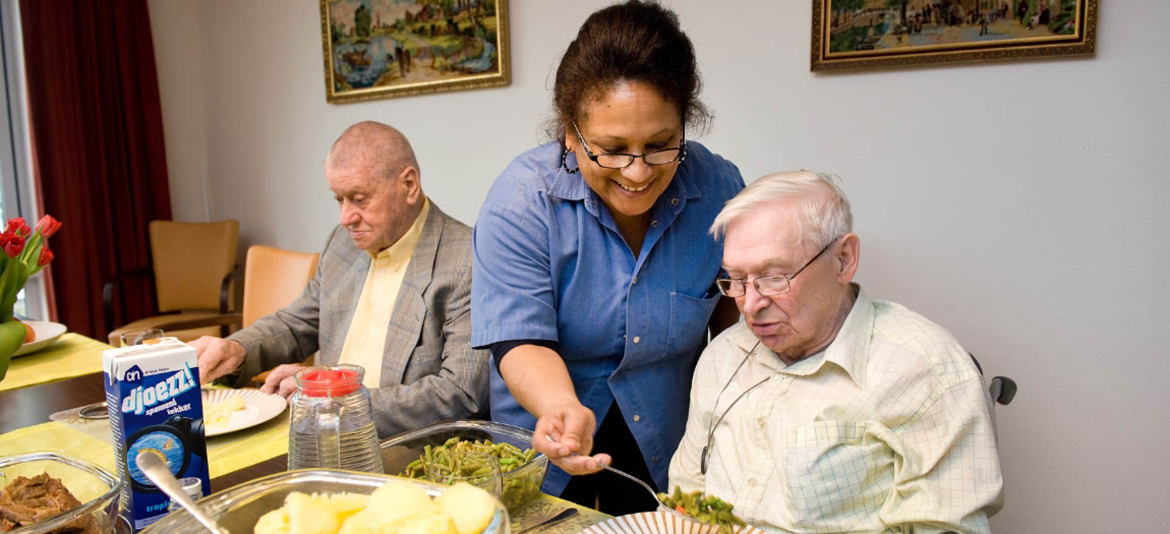 Vrouw schept sperziebonen op aan tafel met 2 oudere mannen, op tafel AH djoezz!