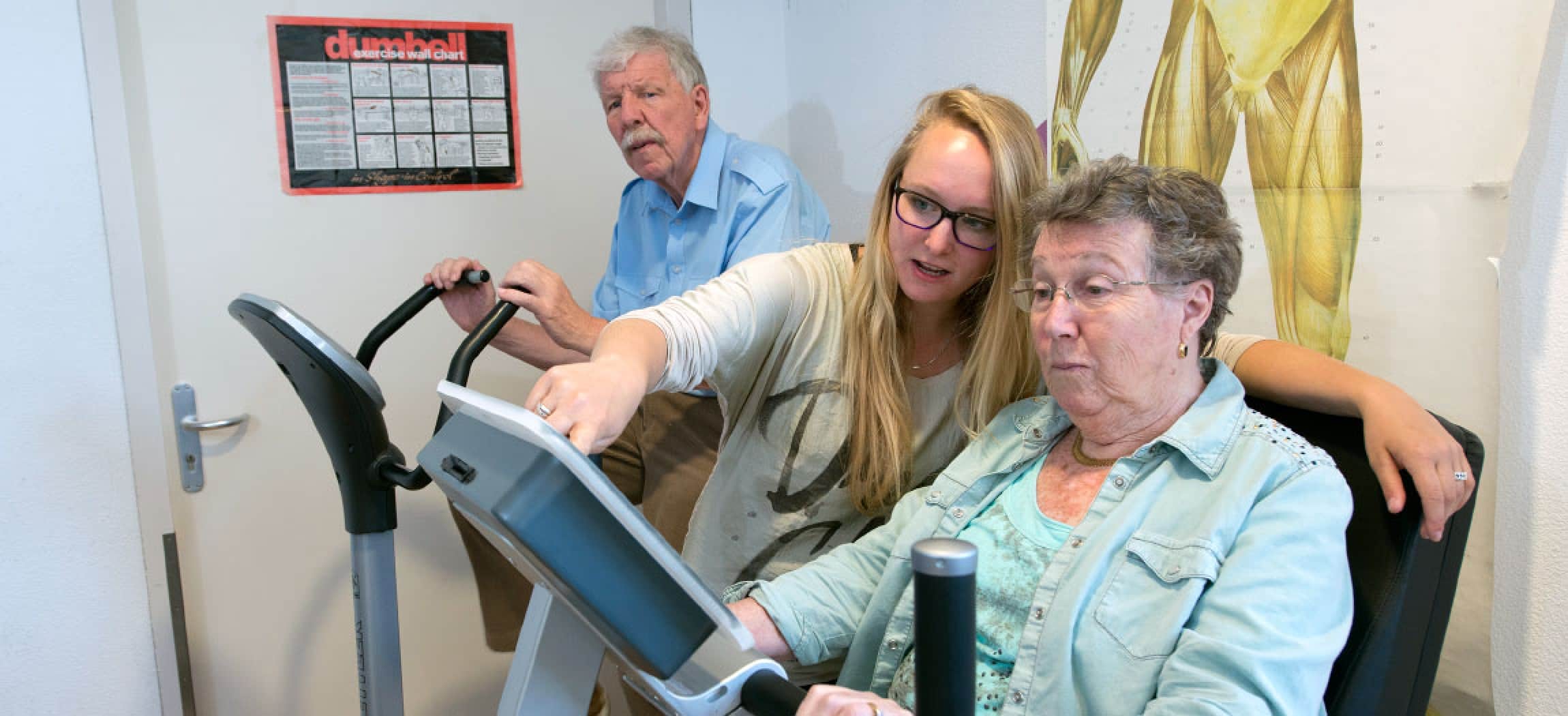 Fysiotherapeut geeft aanwijzingen aan oudere vrouw op hometrainer