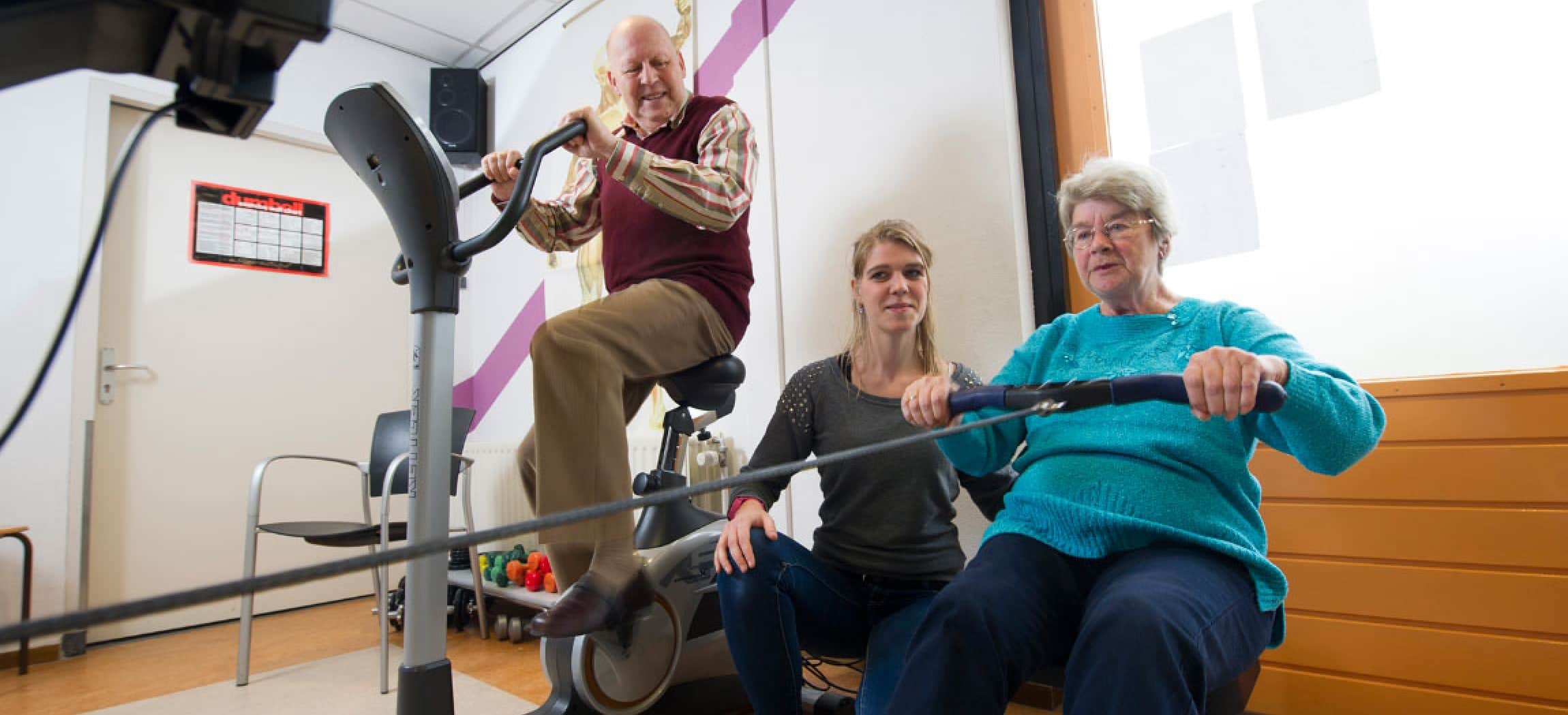 Fysiotherapie oefenen met roeitrainer en fiets fitness apparaat door 2 oudere mensen en fysiotherapeut