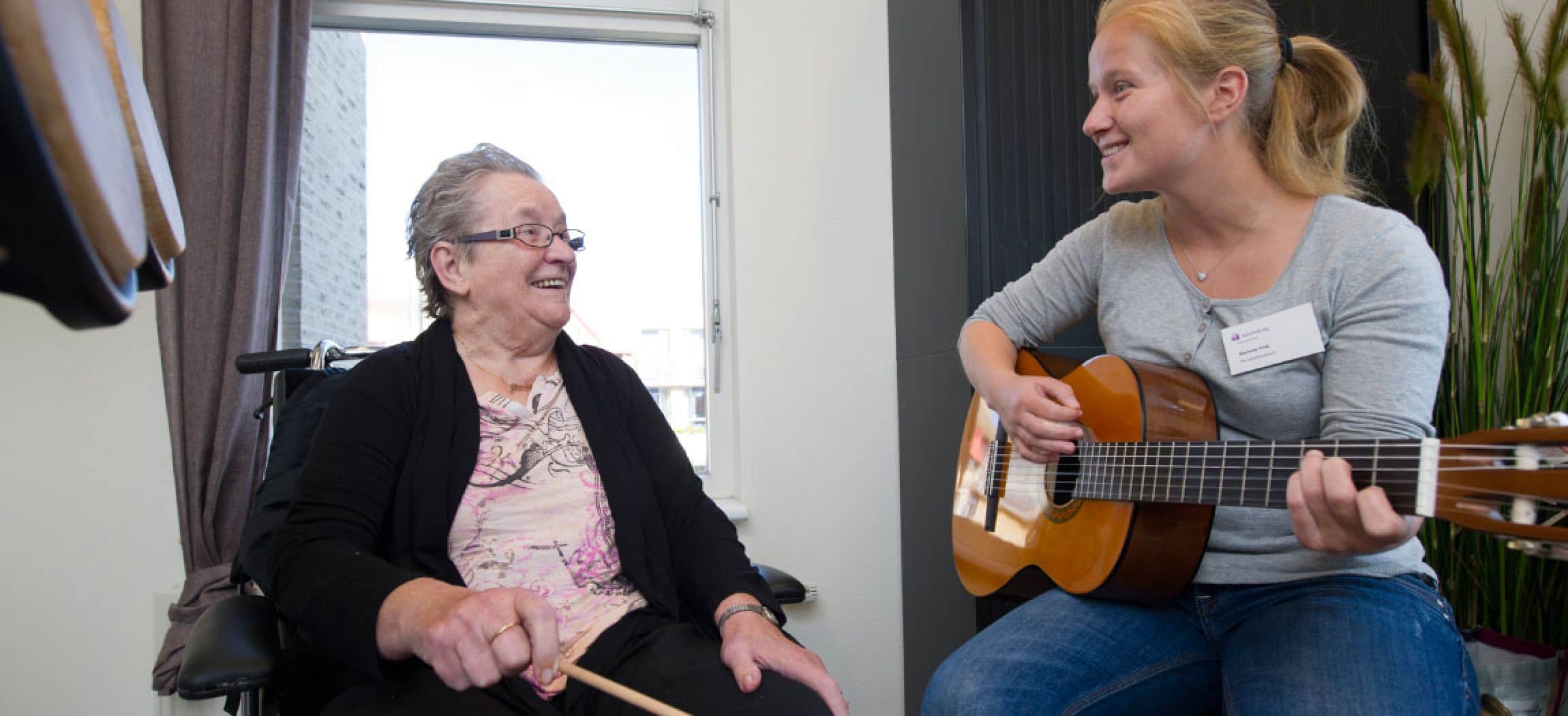 Muziektherapeut speelt op gitaar en zingt voor oudere vrouw in stoel