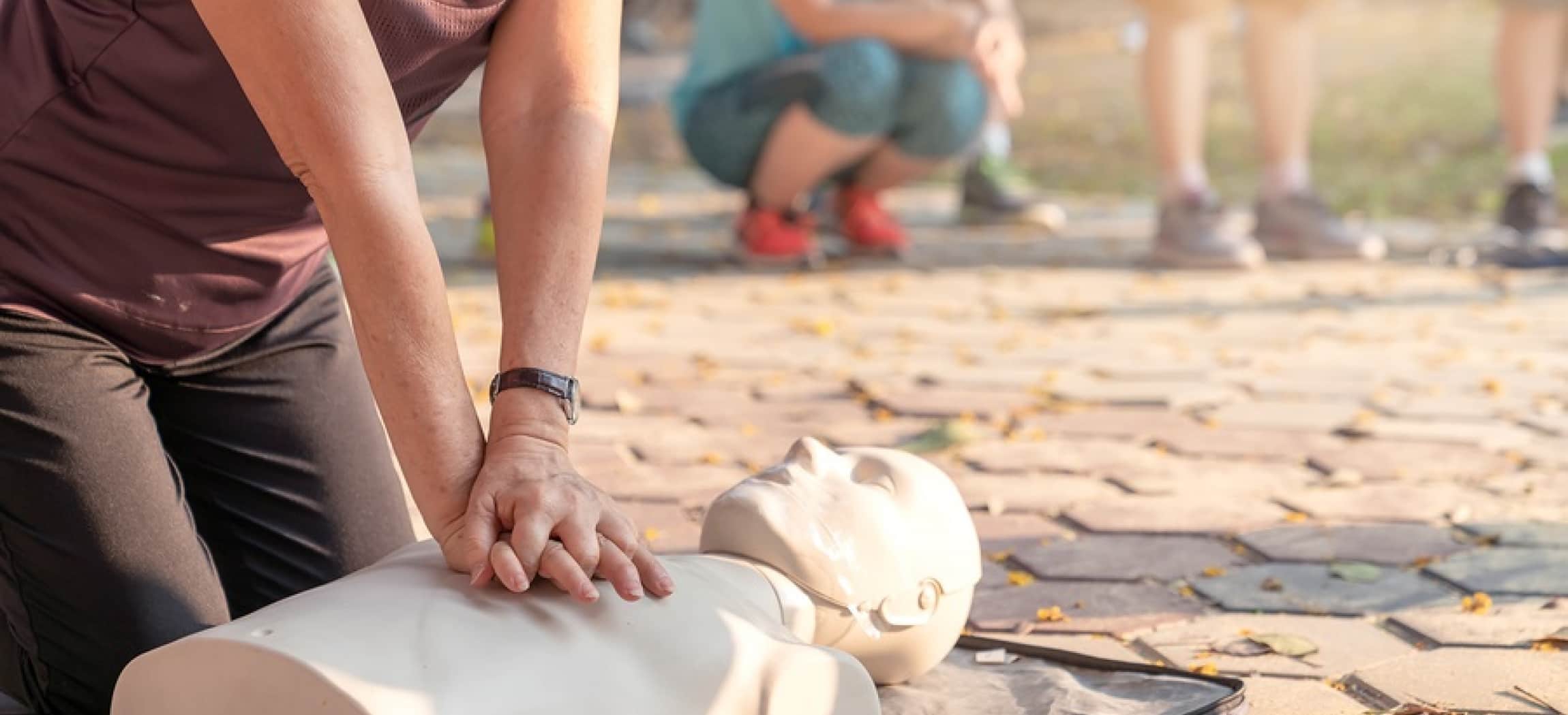 Vrouw knielt op grond en geeft hartmassage aan oefenpop EHBO