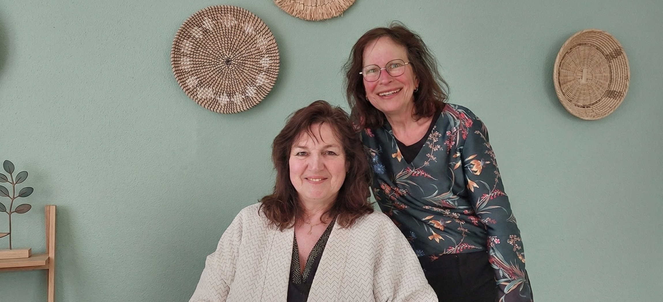 Twee vrouwen bekijken een boekje met poster Schijf van Vijf op achtergrond