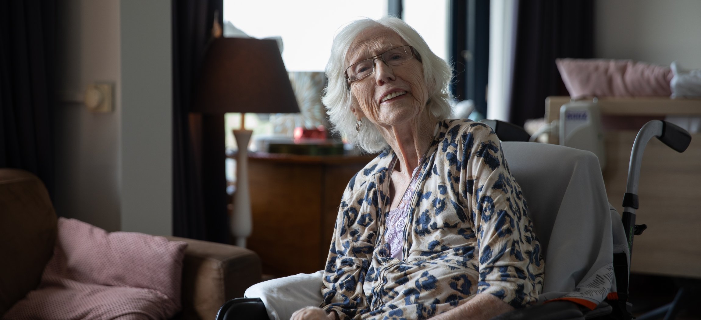 Verzorgende met krullend haar geeft oude vrouw drinken met rietje