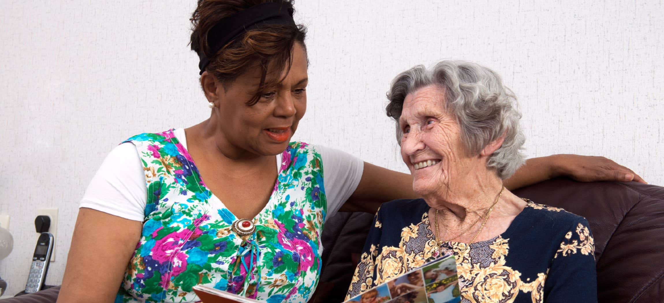 Klassiek ogende oude vrouw leest een tijdschrift samen met andere vrouw met getinte huidskleur