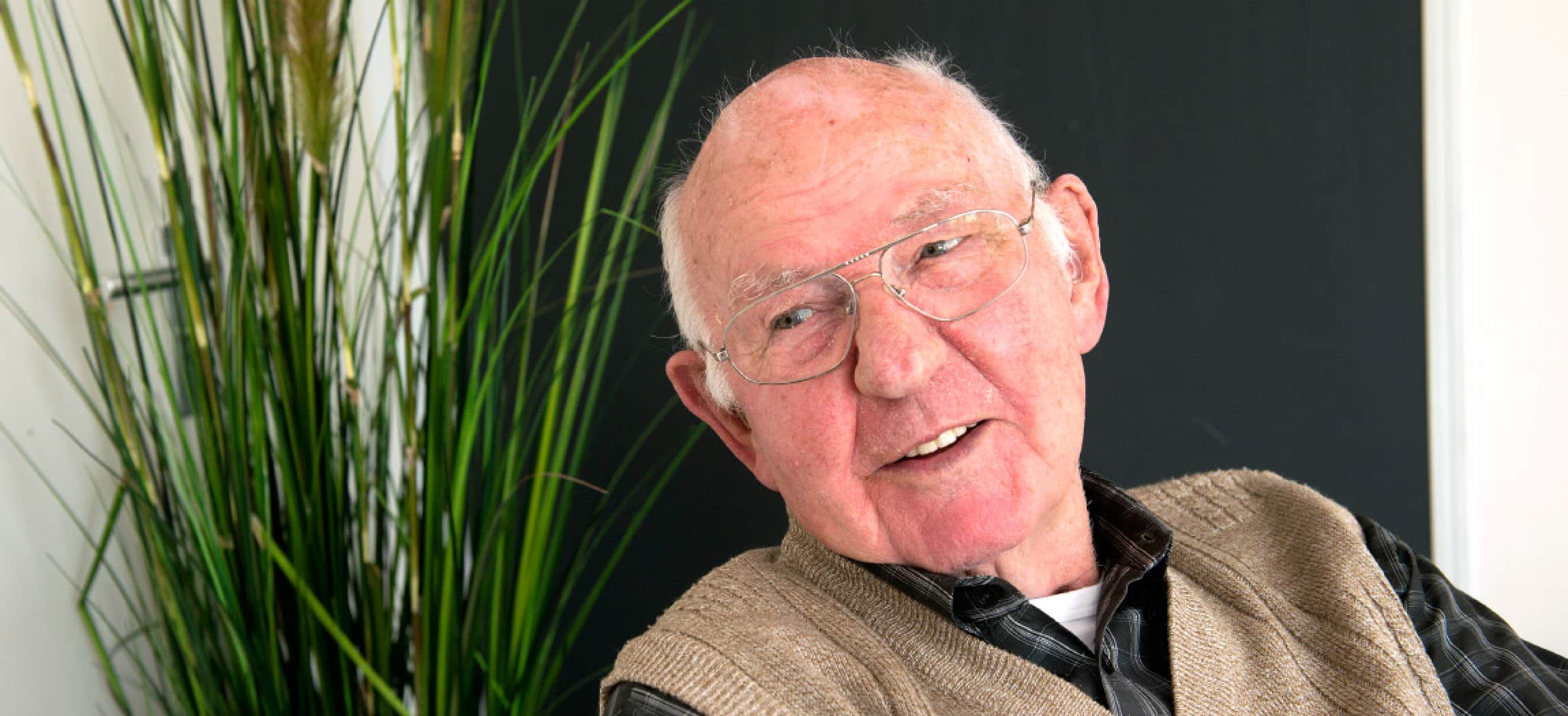 Oude man met bril en bruin vest kijkt vrolijk om