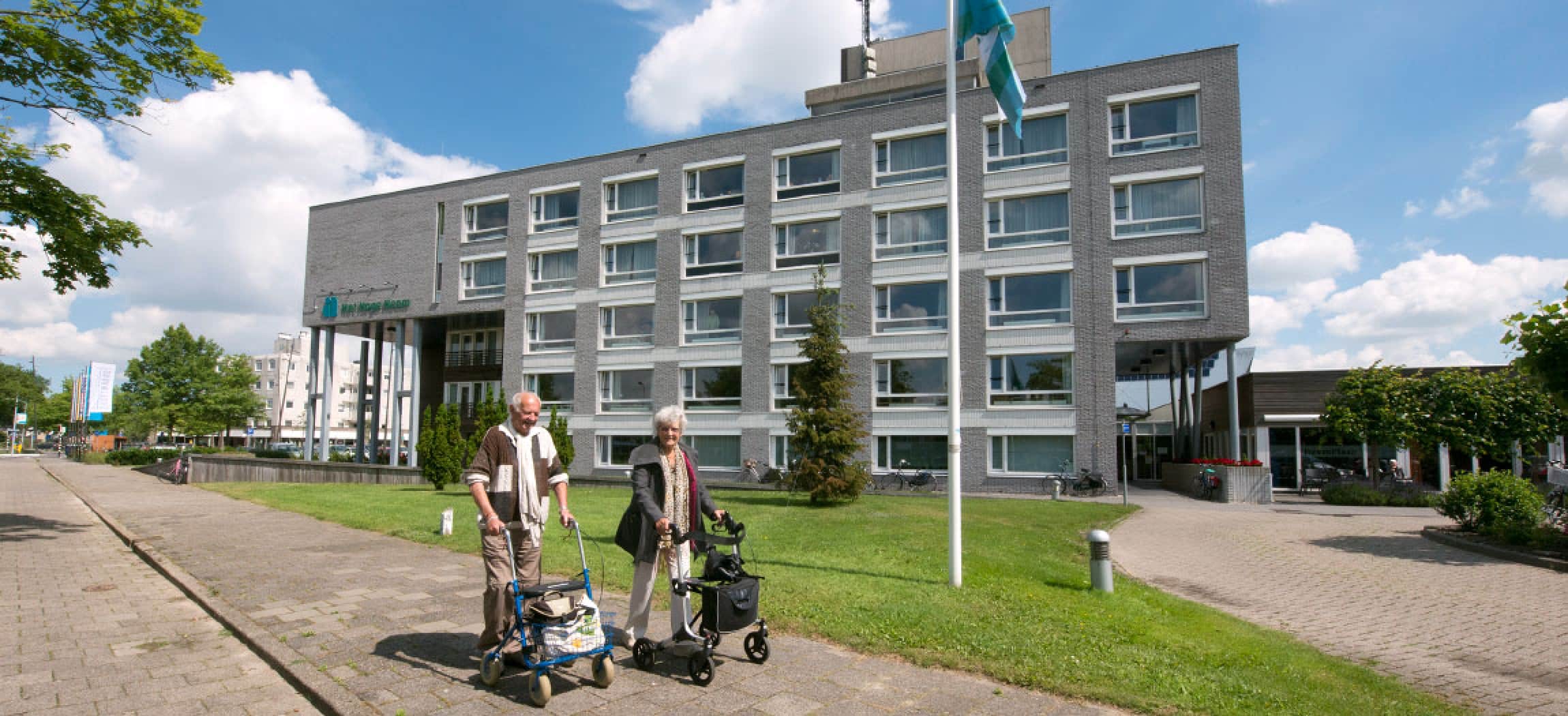Twee bejaarde mensen met rollator lopen op de stoep voor woonzorgcentrum Het Hoge Heem in Uithoorn