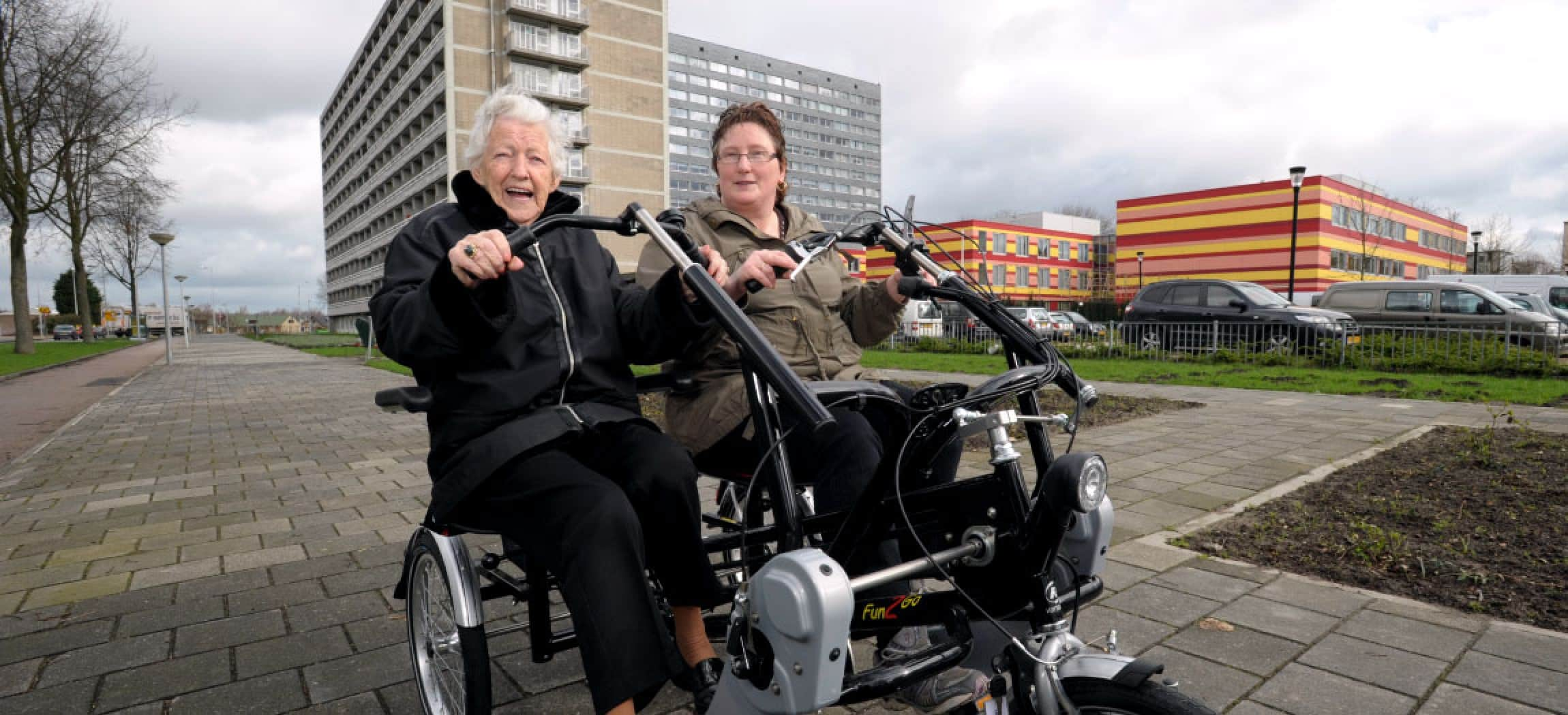 Duo-fiets buiten op de stoep met enthousiaste vrouw en op achtergrond gekleurd gebouw