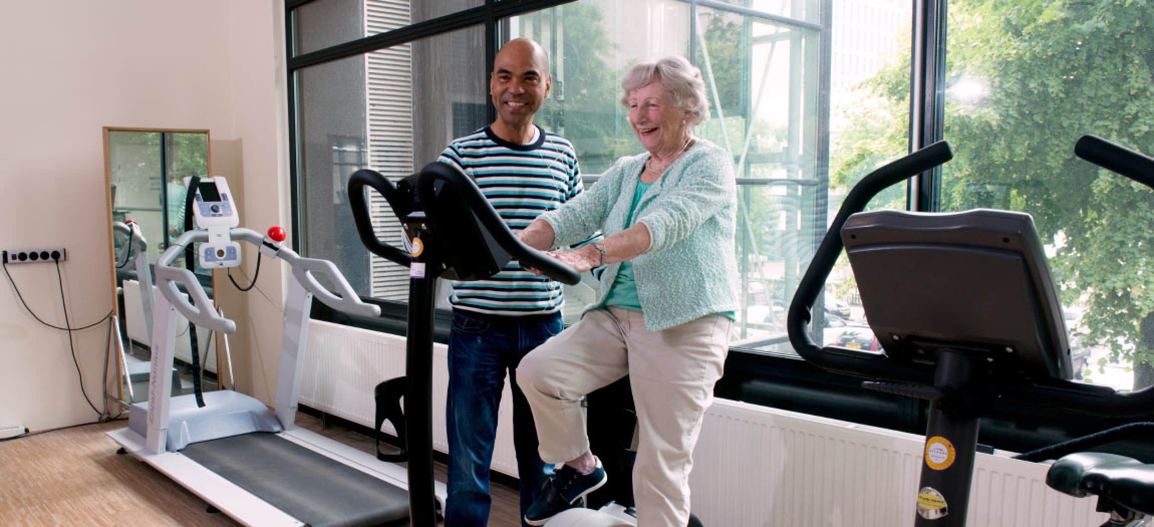 Fysiotherapeut helpt oudere vrouw op fietstrainer ergo