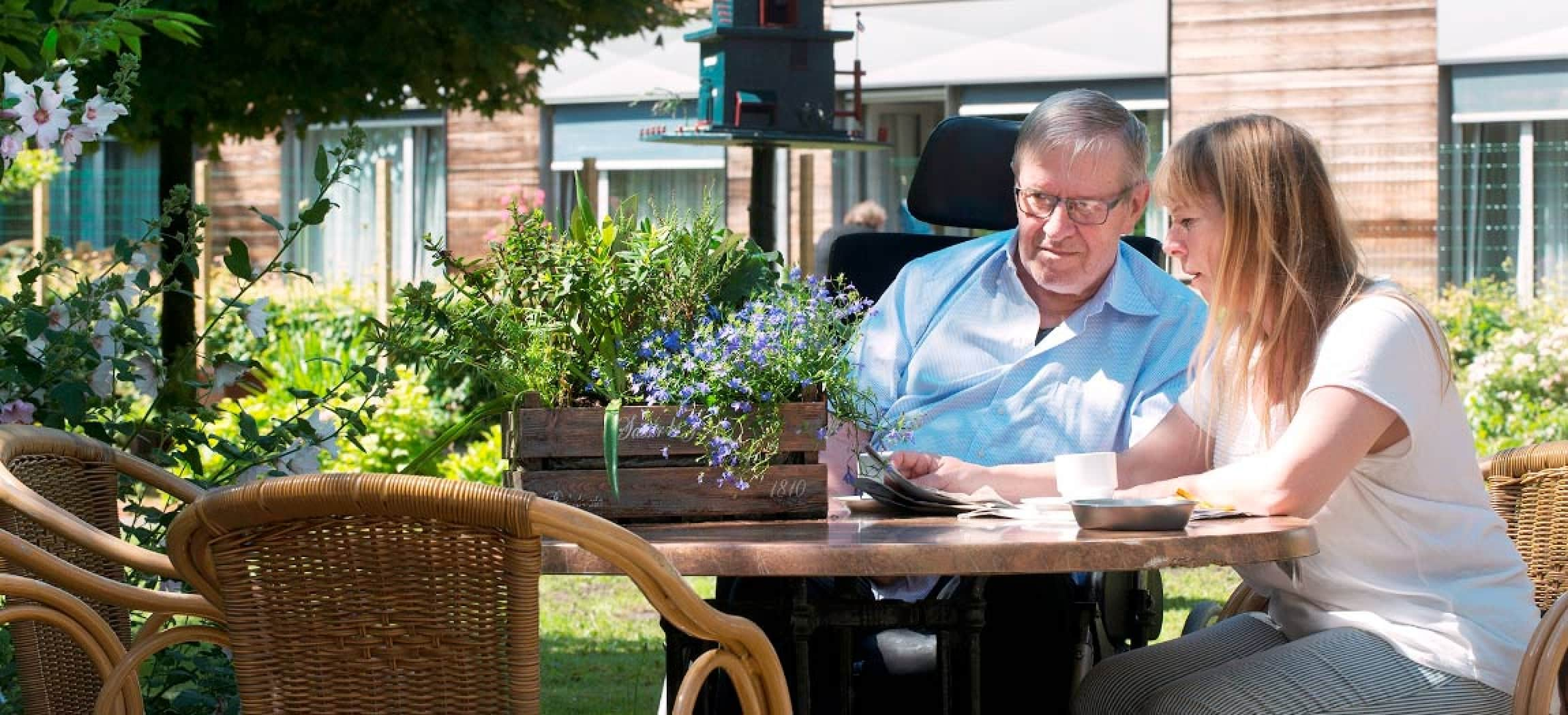 Man in rolstoel en dochter lezen de krant in zonnige binnentuin