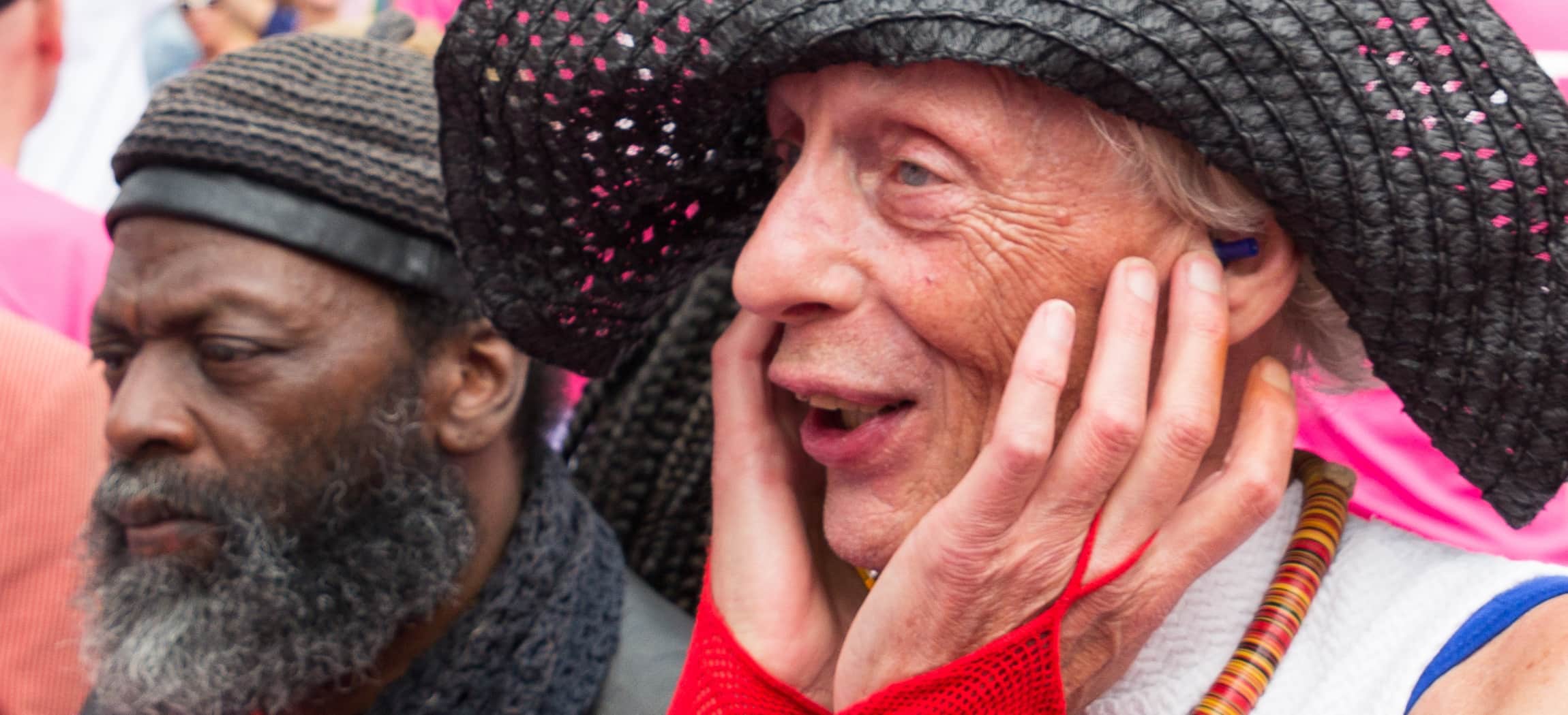 Tijdens Canal Pride kijkt oudere man blij en enthousiast met zwarte flaphoed