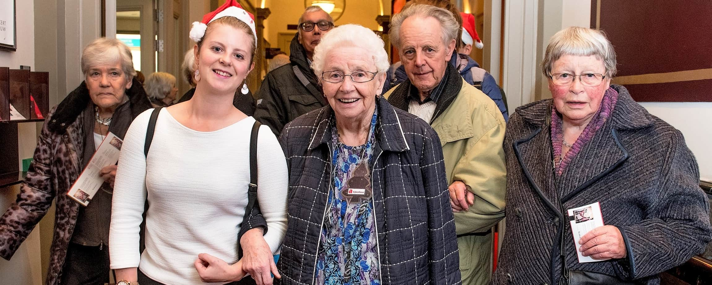 Groep ouderen met jassen aan en een jonge vrijwilliger in Concertgebouw in Amsterdam