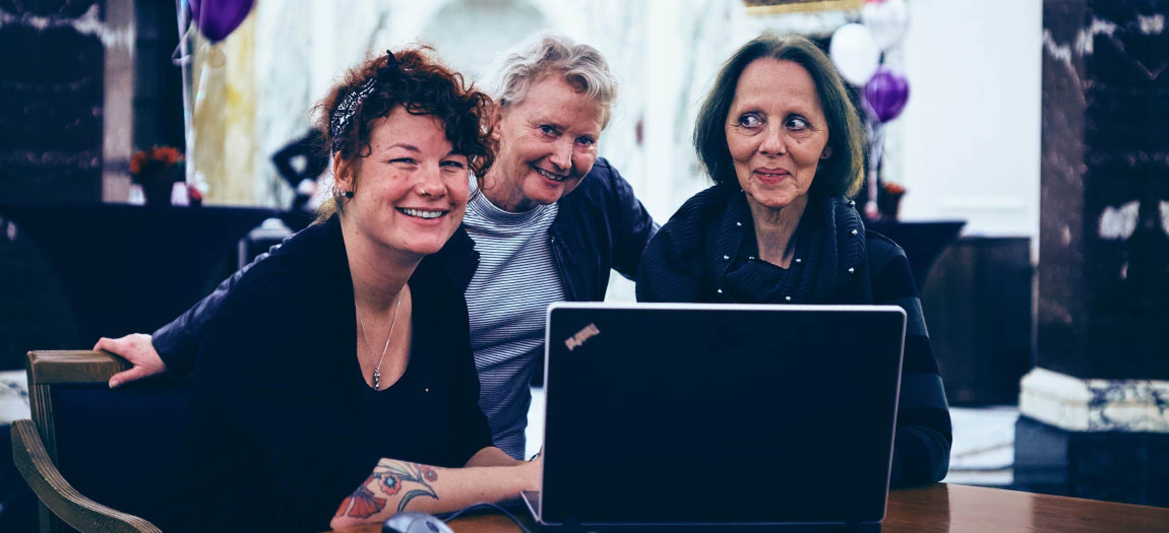 Drie vrouwen achter een laptop in donkere kleding