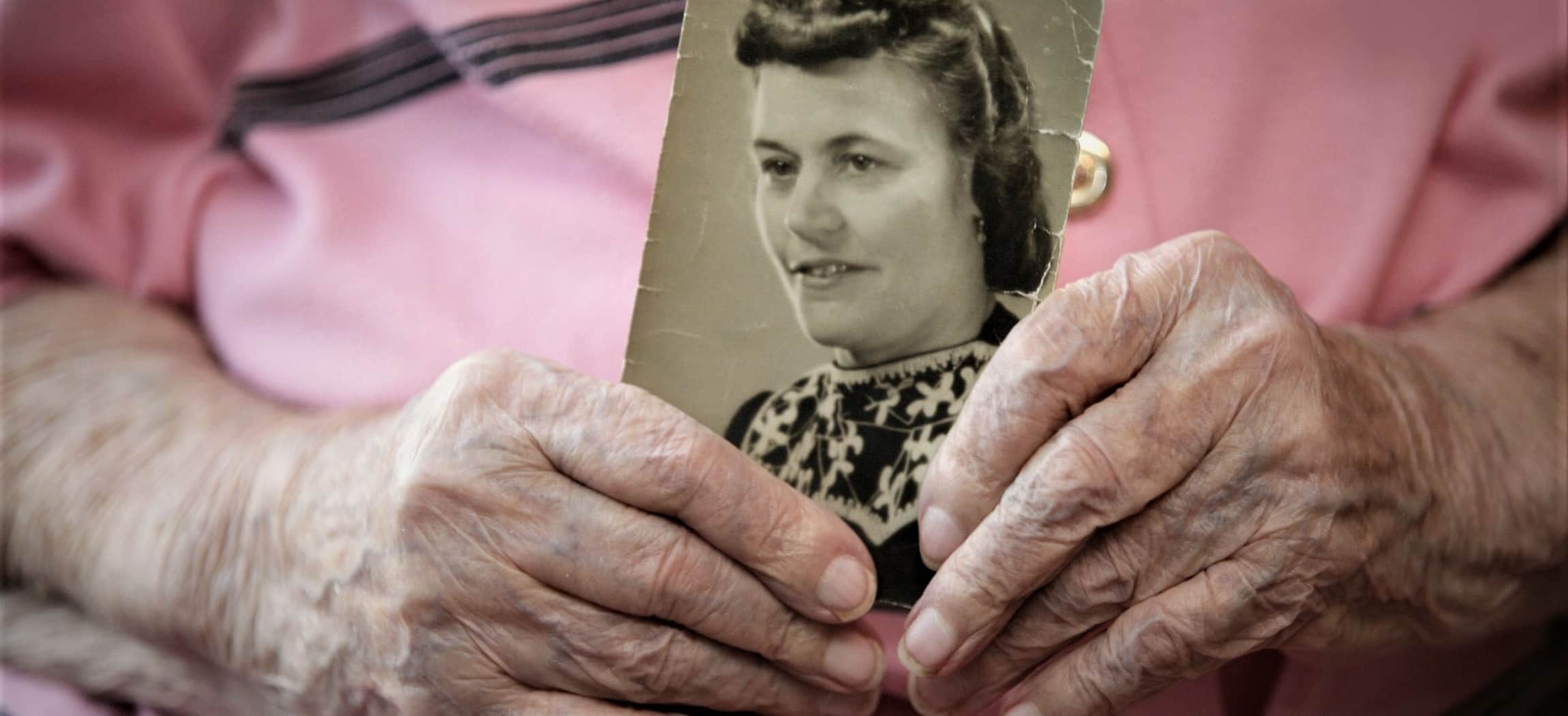 Oude gerimpelde handen houden een klassieke zwart-wit-foto vast, oude vrouw met roze blouse