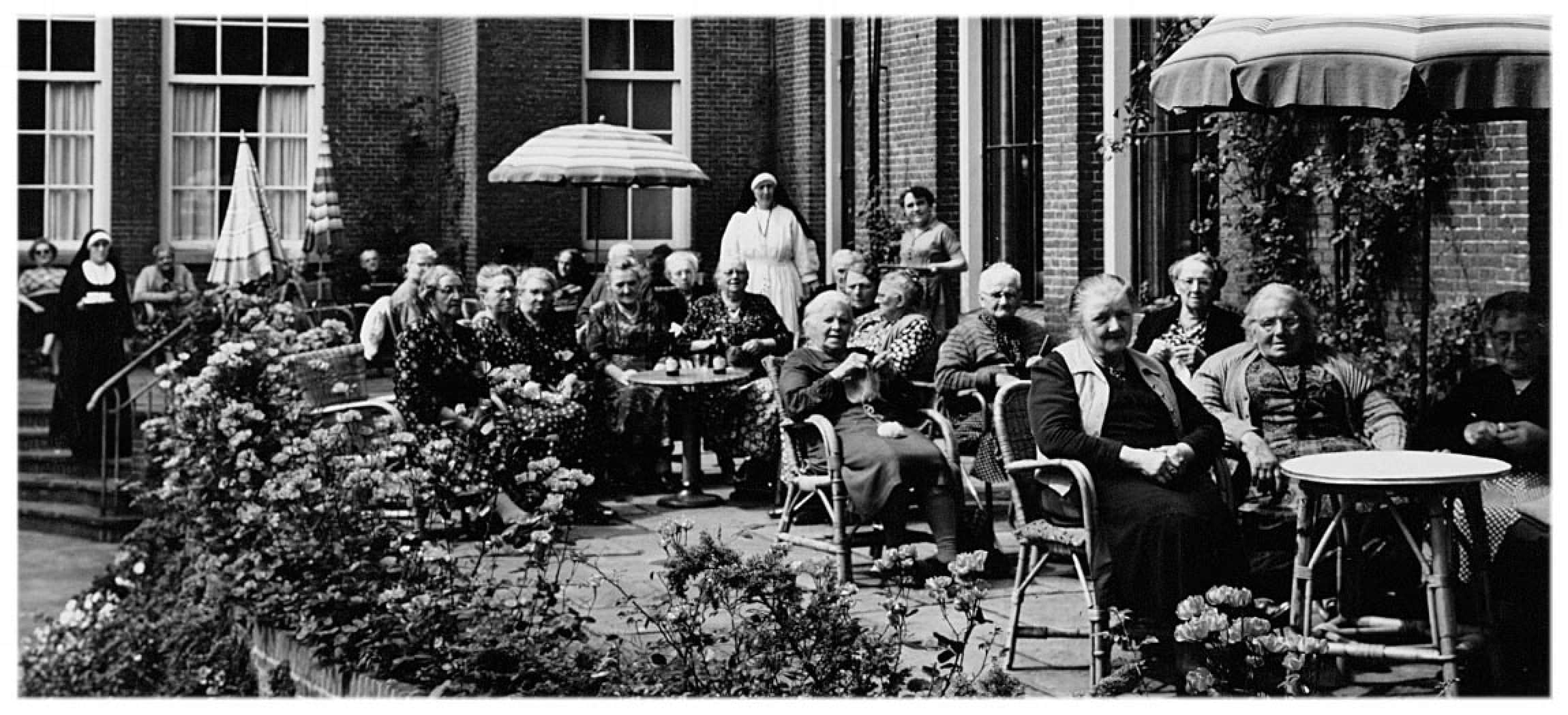 Zwart-wit foto historisch ouderen zitten in binnentuin bejaardenhuis sanatorium met nonnen