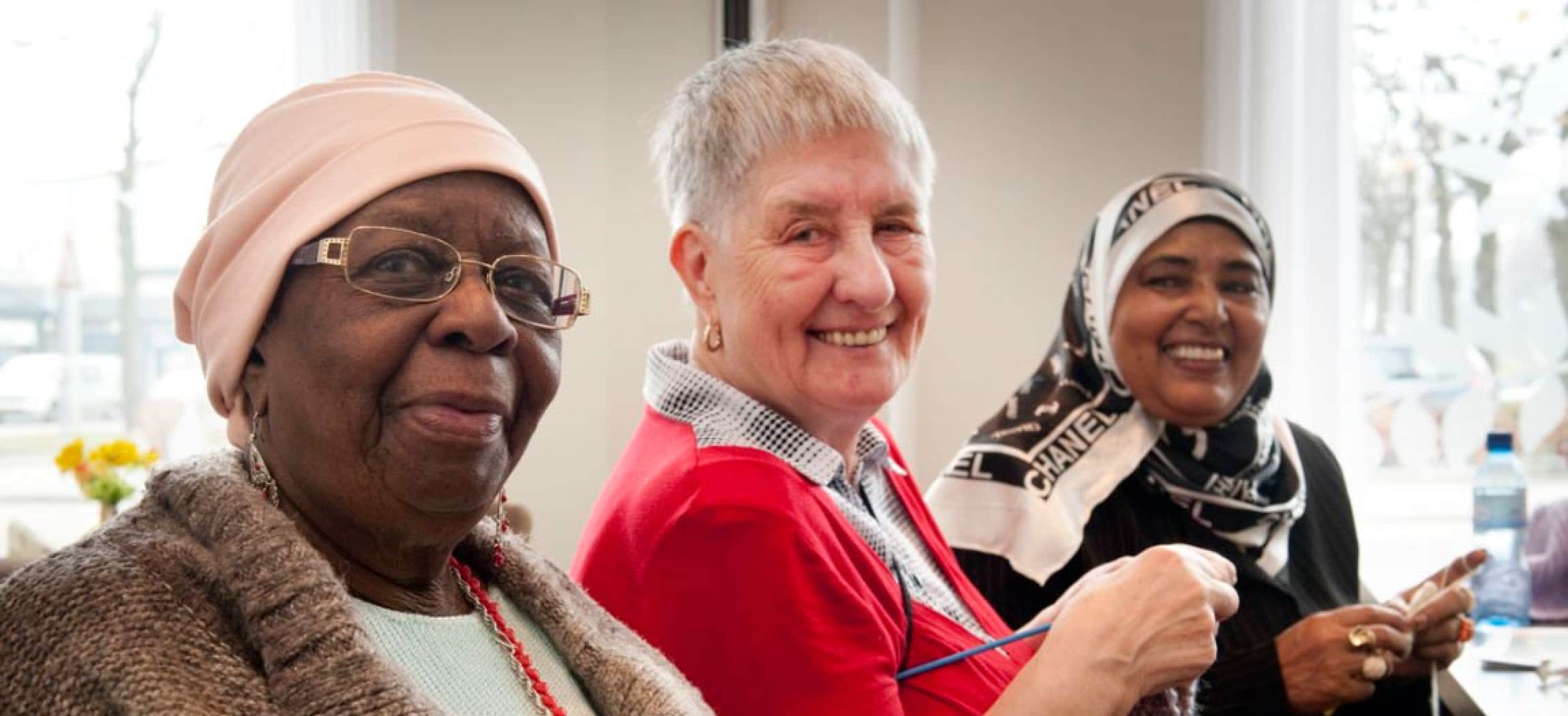 Drie vrolijke oudere dames met breiwerk bij Dagbesteding Amstelring