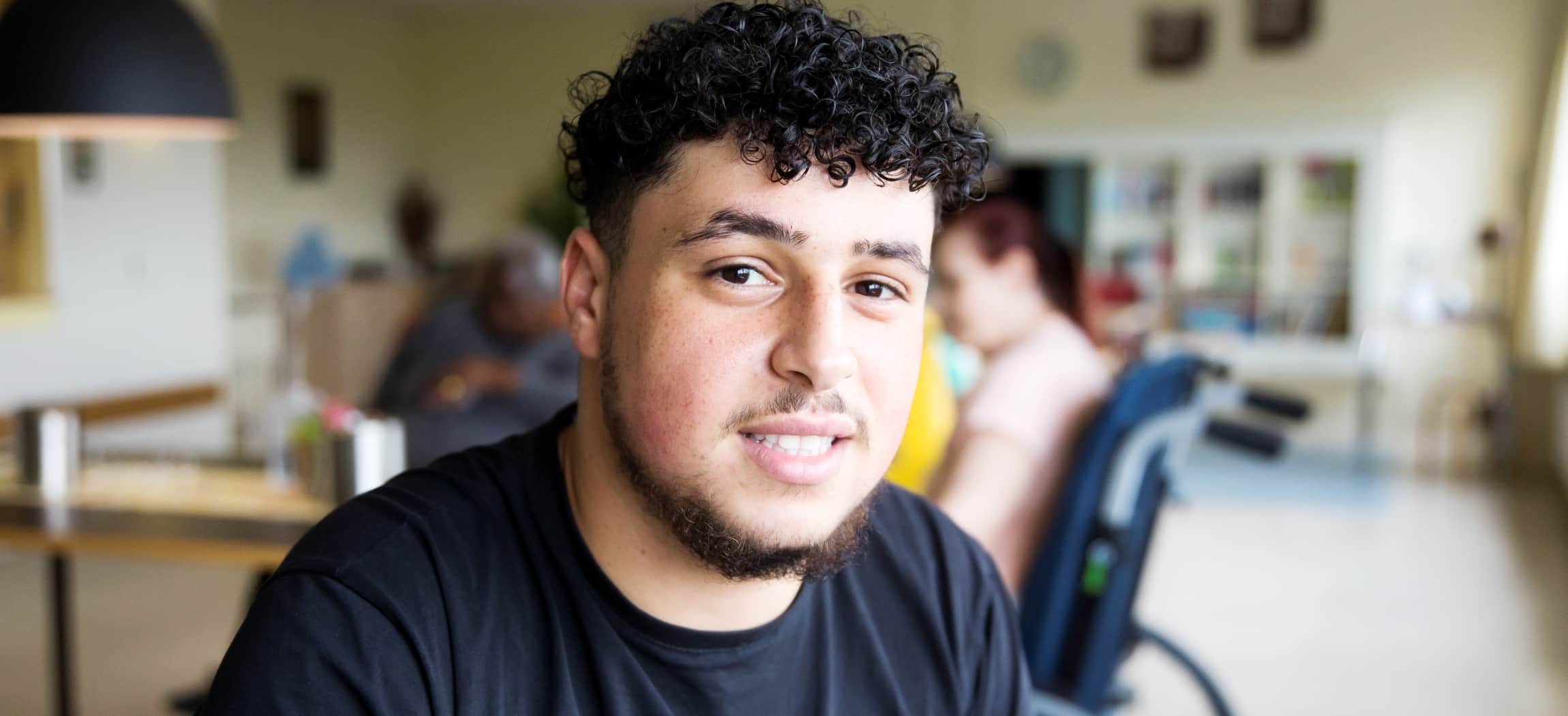 Jonge man met Egyptische uiterlijk in donkerblauw t-shirt, op achtergrond bejaarde mensen