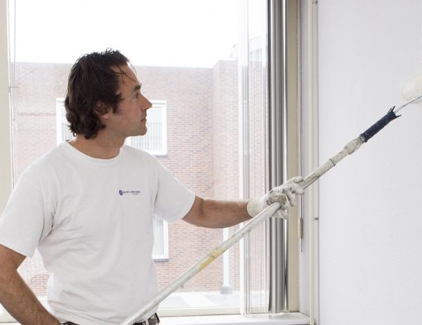 Schilder in wit t-shirt saust een muur wit met een roller op een steel