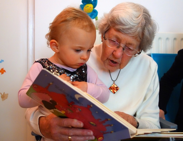 Meisje zit bij oma op schoot en oma leest voor uit een lees- en plaatjesboek