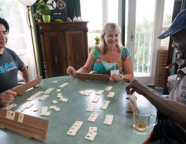 Man, vrouw en oudere man spelen samen Rummikub aan tafel in huiskamer