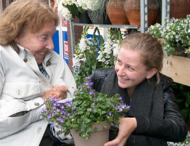 Verzorgster met oudere vrouw in rolstoel bij plantenwinkel