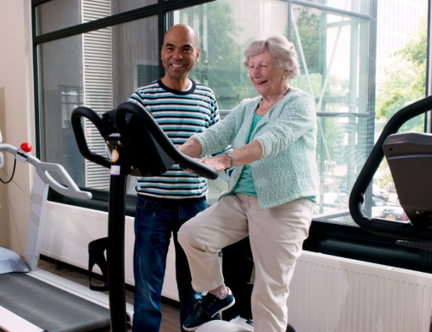 Fysiotherapeut helpt oudere vrouw op fietstrainer ergo