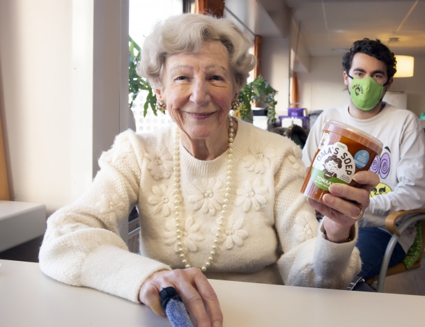 Oudere dame toont pot 'oma's soep' en jonge man zit achter haar