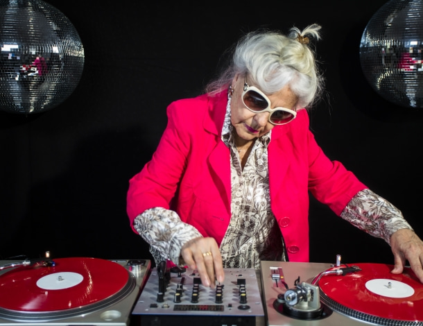 Hippe oudere vrouw aan draaitafel mixt muziek tijdens dansfeest voor swingende senioren